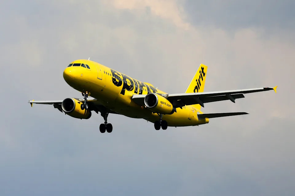 Spirit Airlines yellow plane flying through cloudy skies